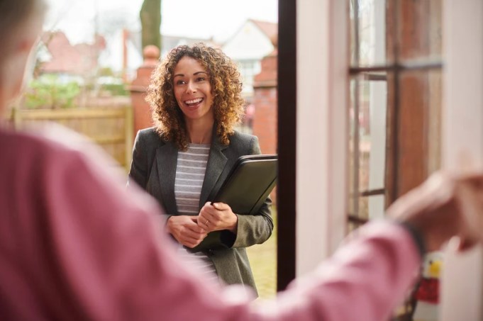 A support worker with a friendly smile stands at the door of a client’s home, holding a folder, ready to provide housing-related support and care services.