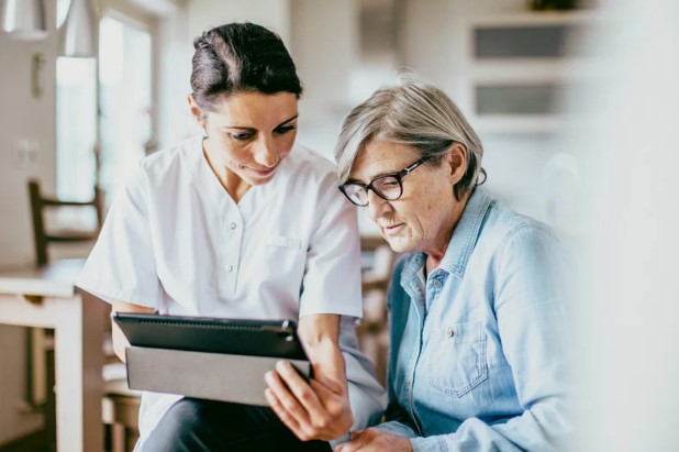 A healthcare professional assists an elderly woman with care management using a tablet, streamlining support through digital tools in a home setting